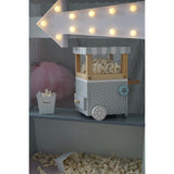 Photo d'une petite machine à pop corn pour enfant en bois posée sur une étagère en dessous d'une grosse fleche lumineuse à empoule. En dessous est disposé une caissette en carton renversée avec des pop corn à l'intérieur
