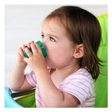 Photo d'un enfant entrain de boire dans un verre de couleur verre. L'enfant est assis sur une chaise haute dont le dossier est vert
