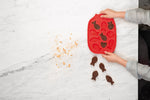 Photo prise par le haut d'une table en marbre avec les mains d'un enfant qui démoule des petits gâteaux au chocolat en forme de poisson. le moule est en silicone de couleur rouge