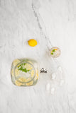 Photo prise par le haut d'une table en marbre avec posé dessus un recipient contenant de la citronade. il y a un verre sur le coté ainsi qu'un citron jaune entier
