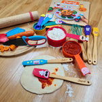 Photo d'un plan de travail de cuisine avec posé dessus plusieurs ustensiles de cuisine pour enfants. il y a un couteau, des tasses à mesurer, des ustensiles et un livre. Les ustensiles sont colorés et représente des personnages