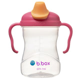 Tasse pour enfant avec sa base transparente et son couvercle avec poignée de couleur rose. il y a une petit bec transaparent et son couvercle amovible de couleur orange