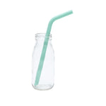 Petite bouteille en verre avec posé dedans une paille de couleur vert d'eau. La photo est prise de face et elle est sur un fond blanc