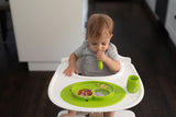 Photo d'un bébé assis sur une chaise haute, en train de manger dans un set de table vert avec son gobelet assortit