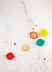 Photo prise par le dessus d'une table de cuisine en marbre avec posé dessus des petits moules de couleurs differents : Rouge, vert et jaune. Avec a l'interieur pour certain des gateaux. On voit dans le fond des moules des formes de tête d'animaux
