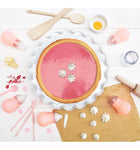 Plan de travail cuisine avec une tarte rose et ses meringues blanches, avec ustensiles de pâtisserie
