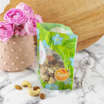 Photo d'un sac à gouter de la marque squiz avec à l'interieur des fruits secs. Le sac est posé sur une table avec un vase et des fleurs