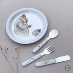 Photo d'une table grise avec posé dessus une assiette avec un dessin d'un ours et d'une petite souris, a coté sont posés des couverts pour enfants aux même couleurs que k'assiette. Il y a une cuillère, une fourchette et un couteau