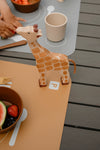 Gros plan sur une girafe en jouet en bois posé sur un emplacement parking d'un set de table de couleur moutarde