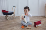 Jeune enfant de 2 ans qui jou à la poupée avec une peluche en forme de lapin, il est entrain de lui donner à boire. L'enfant est assi par terre avec des jouet d'imitation autour de lui representant un sac à langer et de la dinette.