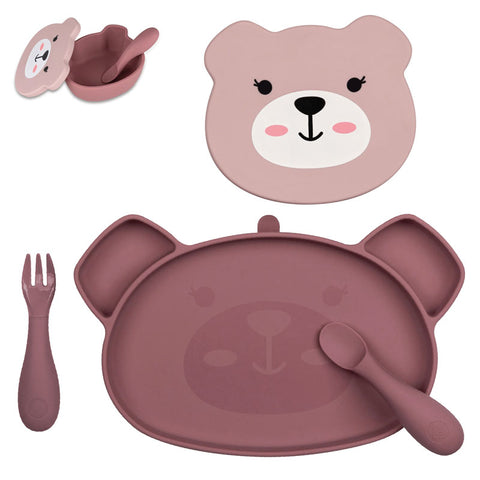 Bol pour enfant de couleur Rose avec une forme de tête d’ours. Le bol est posé sur un fond blanc. Il est équipé d’ couvercle de couleur rose clair avec des illustrations representant le visage de l’ours. Devant le bol est posée une petite cuillère en silicone.