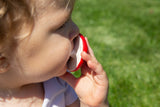 Gros plan sur la tête d'un enfant qui porte à sa bouche un jouet de dentition en forme de champignon rouge et blanc