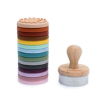 Photo d'un tampon avec manche en bois et a coté de lui des embouts en silicone empilé les un sur les autres de 15 couleurs differentes