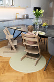 Photo d'une salle à manger vec une table en pierre grise, devant la table il ya 2 chaises hautes en bois avec un enfant de dos sur l'une d'elle. Les chaises sont posées sur des tapis de sol de couleur beige