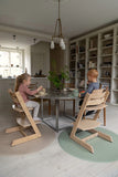 Salle a manger de style scndinave. La table à manger est en marbre, 2 jeunes enfants sont entrain de manger, ils sont assis sur des chaises hautes en bois posées chacune sur des tapis de sol rond de couleur vert et beige