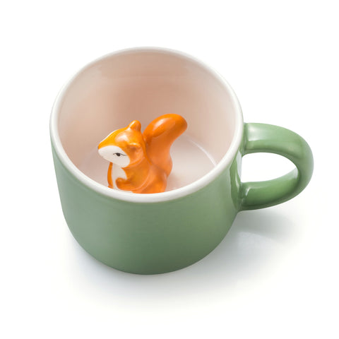 Tasse en porcelaine de couleur verte avec a l'intérieur un écureuil orange en porcelaine. L'intérieur de la tasse est blanche. La tasse est posée  sur un fond blanc