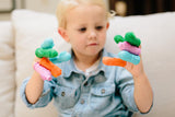 Photo d'un jeune garçon qui tient a chaque doigts des petites marionnettes de couleurs differentes. Les marionnettes sont des brossettes pour les dents