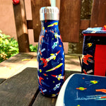 Boite à goûter, gourde et sac isotherme pour enfant posé sur un banc en bois avec en arrière plan un vélo pour enfant. L'ensemble est de couleur bleu nuit avec des illustrations de fusée et d'espace.