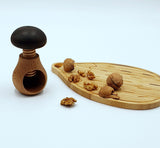 Photo d'un casse noix en forme de champignon posé a coté d'une planche en bois en forme de hérisson, avec posé dessus des noix dont certaine son ouverte, il y a également des cerneaux de noix posés sur la planche et à coté