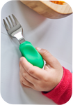 Gros plan sur la main d'un enfant qui tient entre ses doigts une fourchette an inox avec un manche en plastique de couleur vert