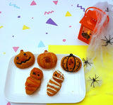 Petits gâteaux d(halloween en forme de momies et de citrouilles. les gateaux sont posés sur une assiette blanche avec  coté un decor d'halloween et des araignés en plastiques